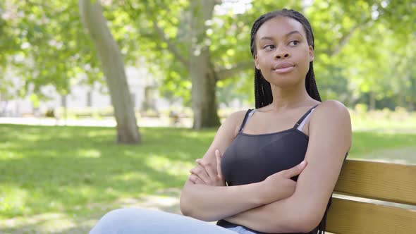 A Young Black Woman Thinks About Something and Sits on a Bench in a Park on a Sunny Day