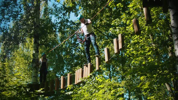Man and Woman Crossing a Construction of the Rope and Stumps - an Entertainment Attraction in the