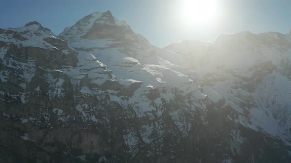 Tilt from snow covered mountains towards a bright sun at a clear blue sky