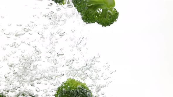 Broccoli falling in water over white