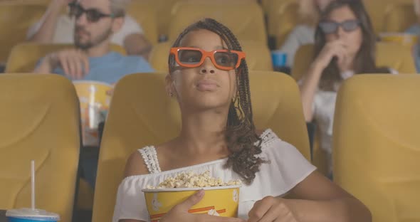 Concentrated African American Girl with Afro Pigtails Sitting with Popcorn in Movie Theater and