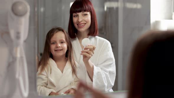 Front View of Happy Woman Cleaning Face of Her Pretty Daughter with Cosmetic and Cotton Pad