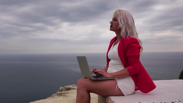 Well Looking Middle Aged Woman Typing on Laptop Keyboard Outdoors on Terrace with Beautiful Sea View