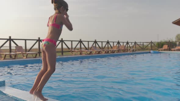 A Girl with Swimming Goggles Jumps Into a Pool with Clear Water on the Background of a Warm Summer