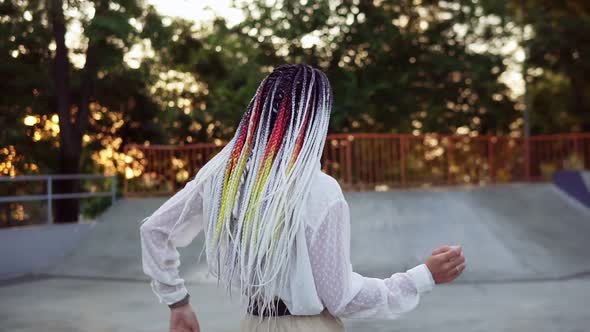 Carefree Woman in Casual with Colorful Dreadlocks Standing in the Center of Outdoors Skatepark