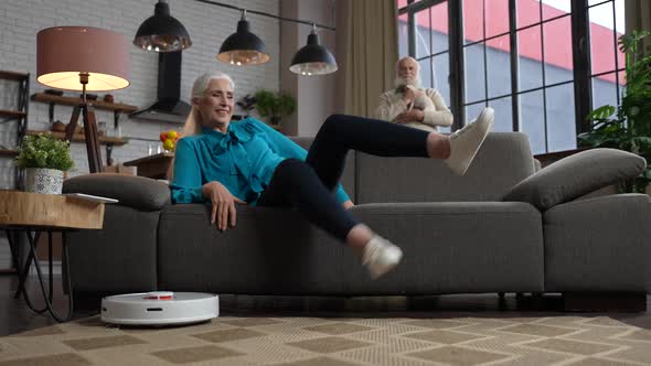 Happy Aged Woman Turning on Robot Vacuum Cleaner