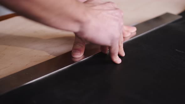 The Tanner Is Cutting Black Leather Sheet with a Razor and Metre