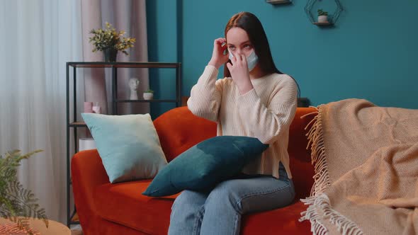 Young Caucasian Sick Woman Wearing Medical Protection Mask Sitting in Living Room Looking at Camera