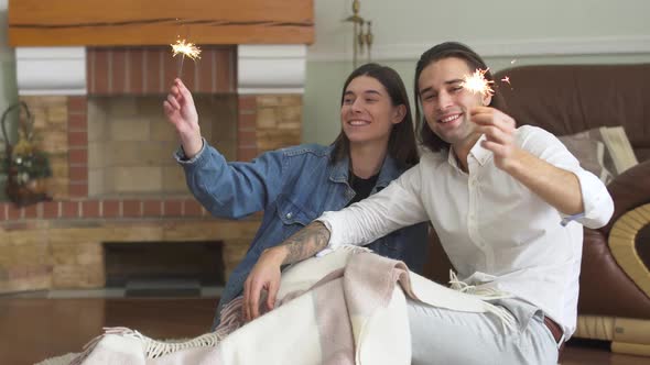 Young Beautiful Couple Man and Woman Sit on the Carpet on the Floor and Light a Sparklers