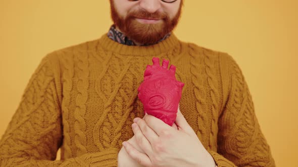 Middleaged Bearded Man Squeezing Red Artificial Heart Model in Front of His Chest Pulse and Healthy