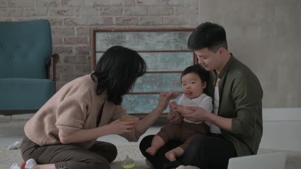 Young asian parents cheerfully feed baby from spoon with delicious puree