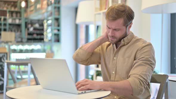 Young Man with Back Pain Using Laptop in Cafe