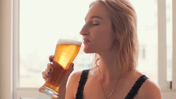 The Woman Is Drinking Light Beer From a Beer Glass and Smiling.