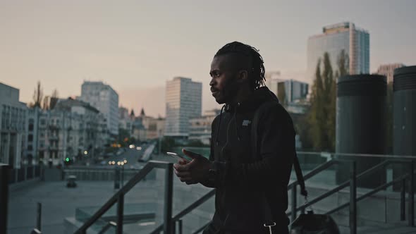 Active African American Guy Going Home in Evening Walking with Smartphone and Sport Bag Tracking