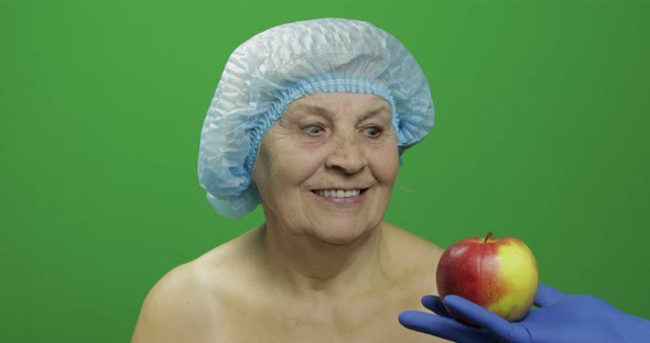 Elderly Female Lady in Protective Hat. Doctor Shows Her an Apple