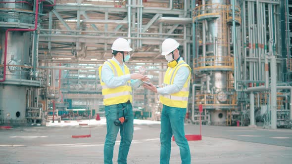 Two Engineers in Face Masks are Talking at the Oil Refinery