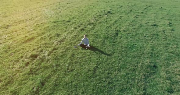 Low Orbital Flight Around Man on Green Grass with Notebook Pad at Yellow Rural Field.