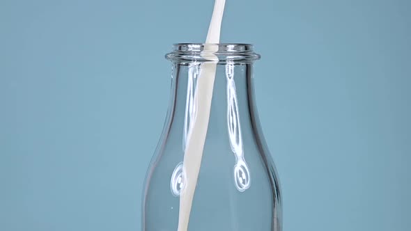 Pouring fresh milk in glass bottle over blue background