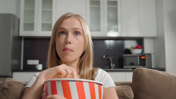 Amazed Blonde Sitting on Sofa with Popcorn and Watching TV