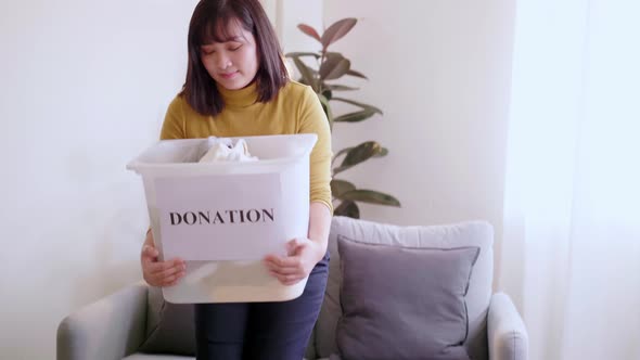 Portrait of Asian young woman looking at camera holding box with clothes for donation. Concept campa