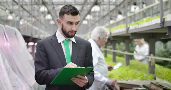 Portrait of Confident Young Caucasian Man Inspecting Glasshouse. Handsome Bearded Auditor Taking