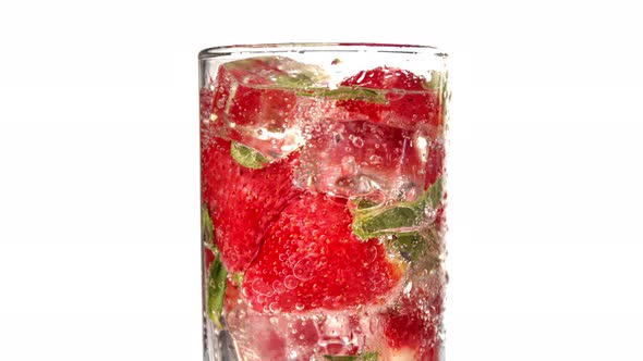 Closeup Rotation Glass of Refreshment Strawberry Mint Ice Cocktail with Bubbles Slow Motion Isolated