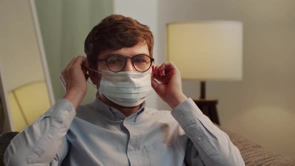 A Young European Man Puts a Mask on His Face While Sitting on the Sofa