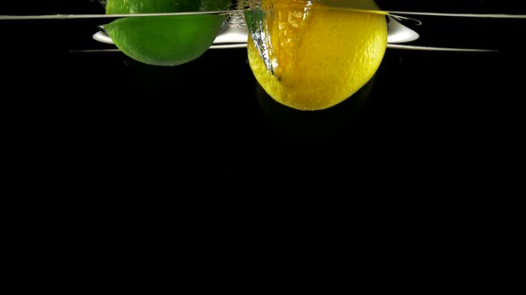 Slo-motion whole lemon and lime falling on water