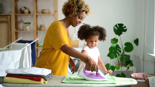 Teamwork of Black Afro Mother and Little Daughter Ironing Linens Clothes Together Spbd