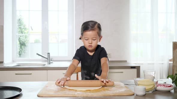 Toddler in Black Shirt Rolls Elastic Dough with Rolling Pin
