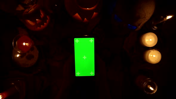 Person Clicks on a Greenscreen Smartphone in Vertical Orientation Among Halloween Decoration