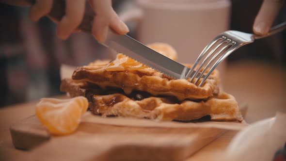 A Woman Cutting a Waffle Covered in Syrup in the Plate