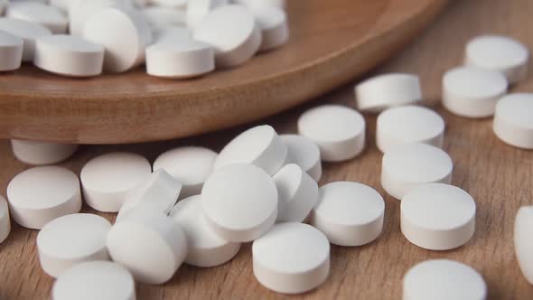 White pills fall on a wooden surface in slow motion next to a wooden spoon.