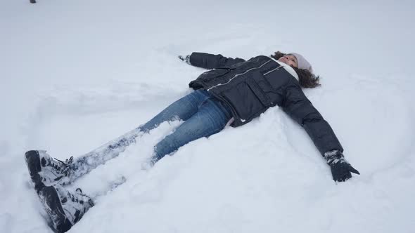 Wide Shot of Carefree Happy African American Teen Girl Making Snow Angel Lying on Snowy Ground in