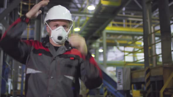 Male Engineer in Hardhat and Respirator Walking along Production Line