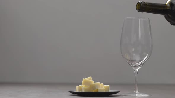 Slow Motion Pour Red Wine Into Wineglass with Hard Cheese on Background on Wood Table