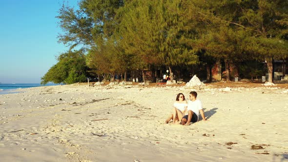 Traveling couple exploring white sandy beach of tropical island with pine trees during their vacatio