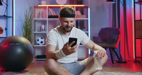 Guy in Sportswear Sitting on the Floor with Crossed Legs, Drinking water