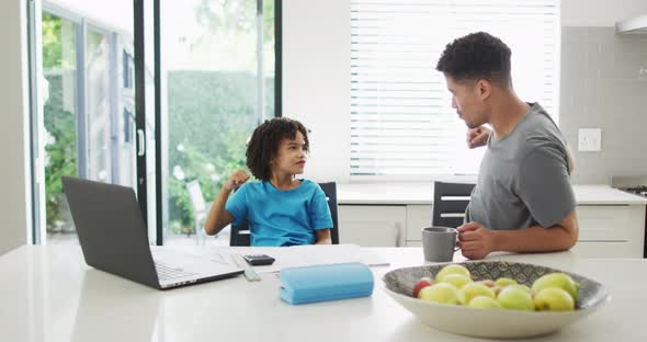 Happy biracial man and his son doing homework together, fistbumping