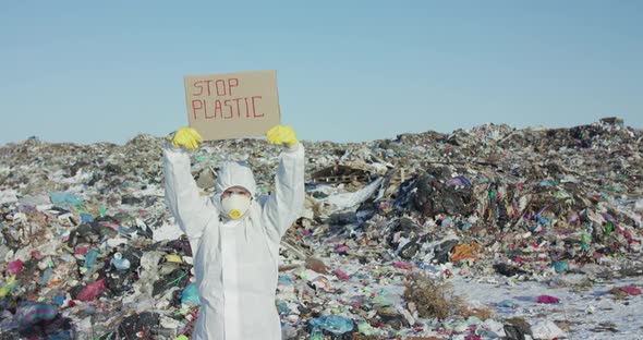 Man in Protective Suit Show Protest Sign "Stop Plastic" at Huge Plastic Landfill