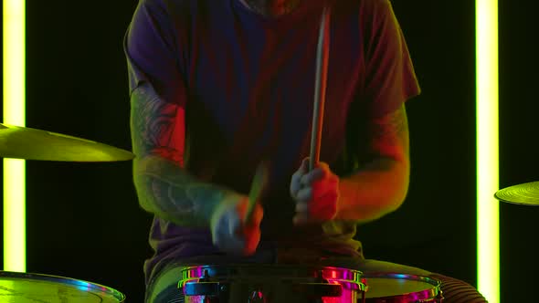 Skilled Man Musician Plays Contemporary Drum Kit in a Dark Studio Illuminated By Multicolored Neon