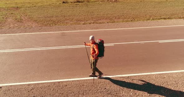 Flight Over Hitchhiker Tourist Walking on Asphalt Road. Huge Rural Valley at Summer Day. Backpack