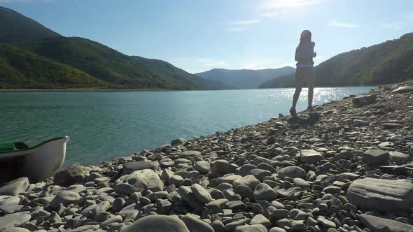 Young Woman Jogging Along Pebbled Sunlit Riverbank in the Mountains on Sunny Day