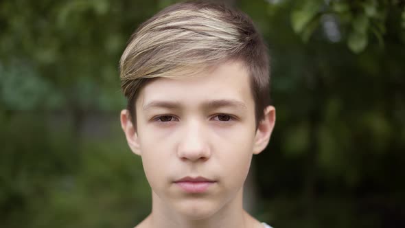 Sleepy Portrait of a Boy with a Stylish Hairstyle Looking at the Camera and Smiling Outdoors