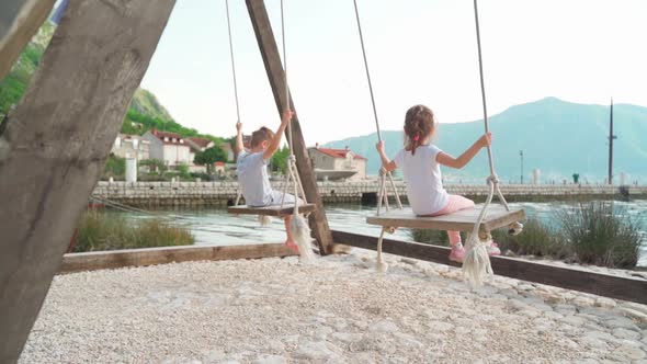 A Girl and a Boy Swing on a Swing Near the Sea with a Beautiful View of the Bay and Mountains