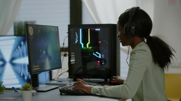 Excited Black Woman Gamer Sitting on Desk Having Headset with Mic Playing