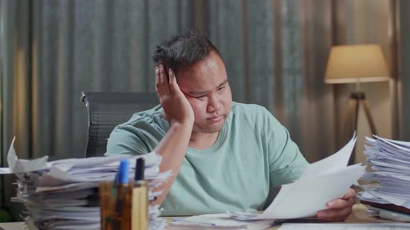 Close Up Of Fat Asian Man Yawning And Putting Hand On Cheek While Working Hard With Documents