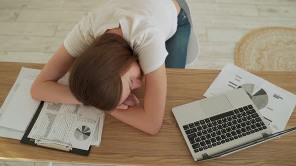 Young Tired Woman Sleeping at Her Office Desk Near the Laptop