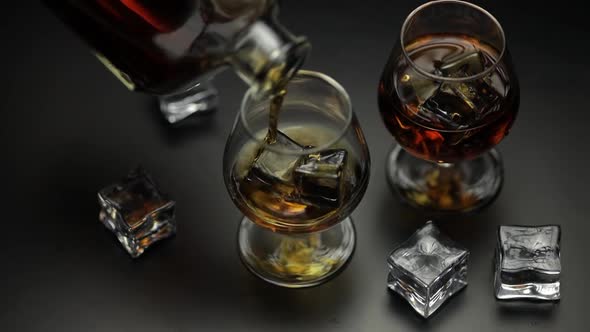 Pouring Alcohol Drink Whiskey, Cognac Into Glass with Ice Cubes. Slow Motion