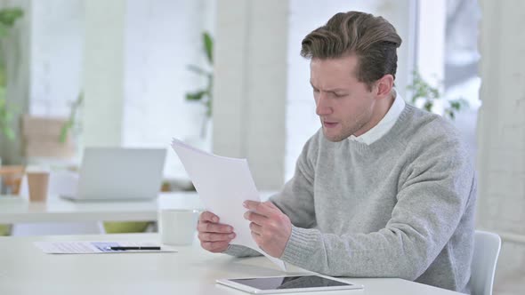 Disappointed Creative Young Man Reacting To Failure on Documents 